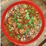 A red bowl with braised short ribs in it topped with chopped parsley